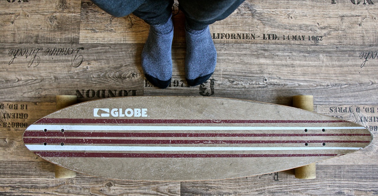 grey wooden longboard on the floor with a person sitting beside it